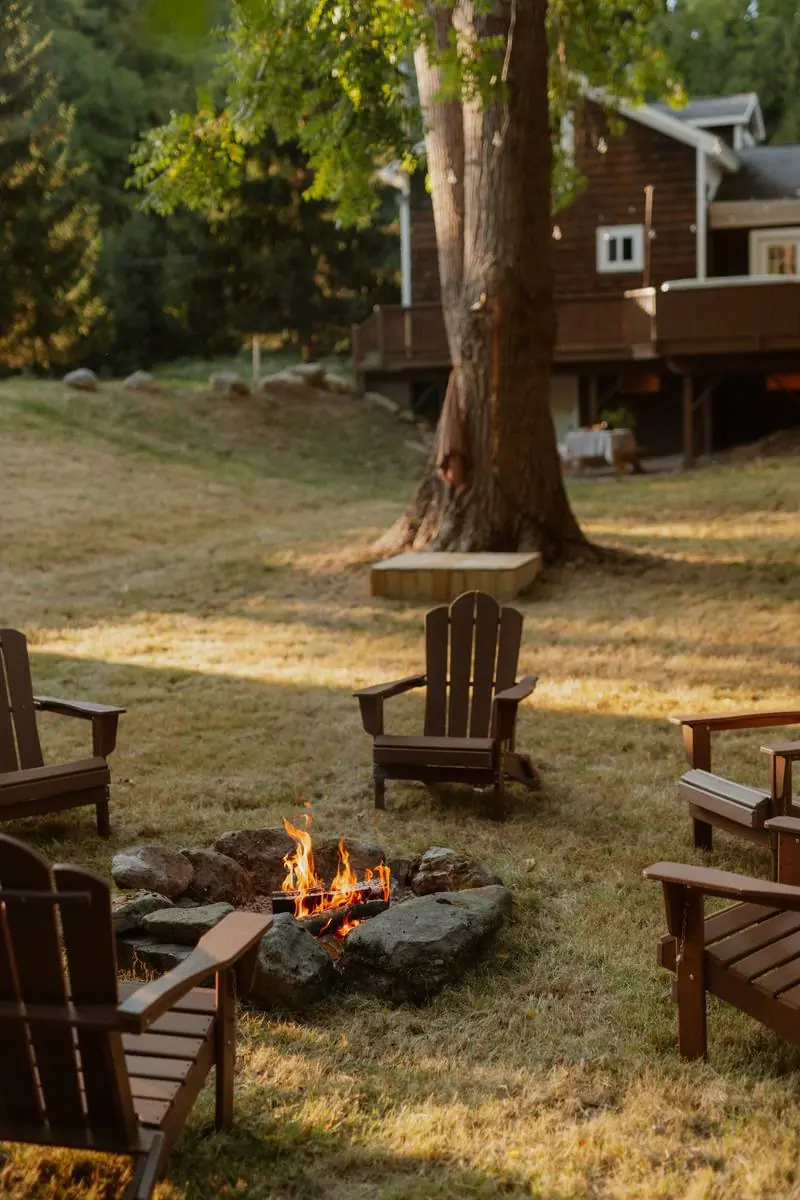 Adirondack chairs around a fire pit on a lawn, a deck behind.
