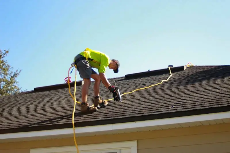 A roofer working on a residential asphalt shingle roof.